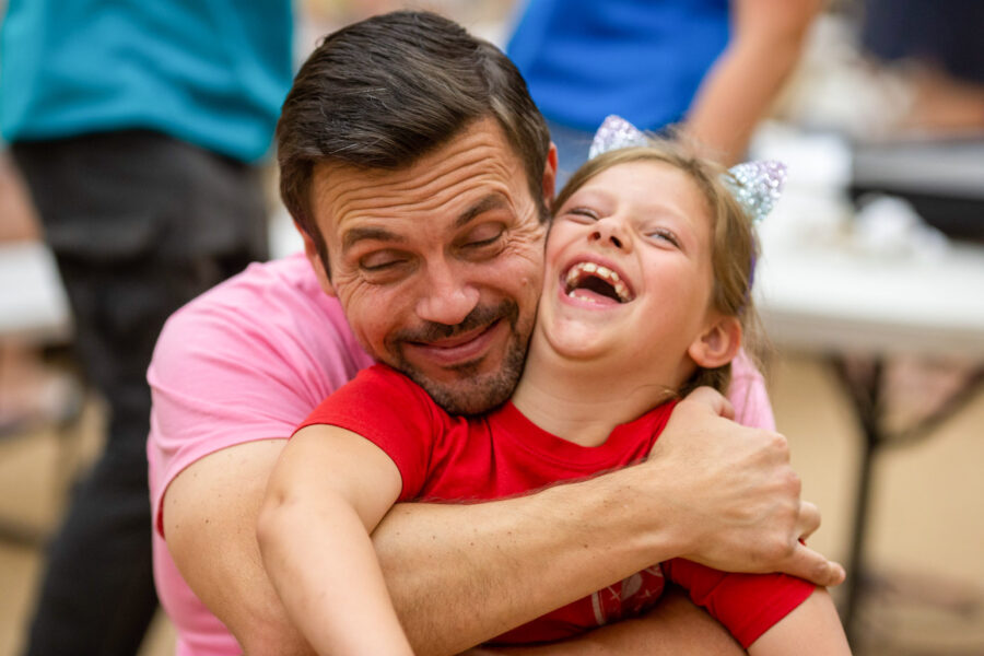 man smiling and hugging a laughing girl.