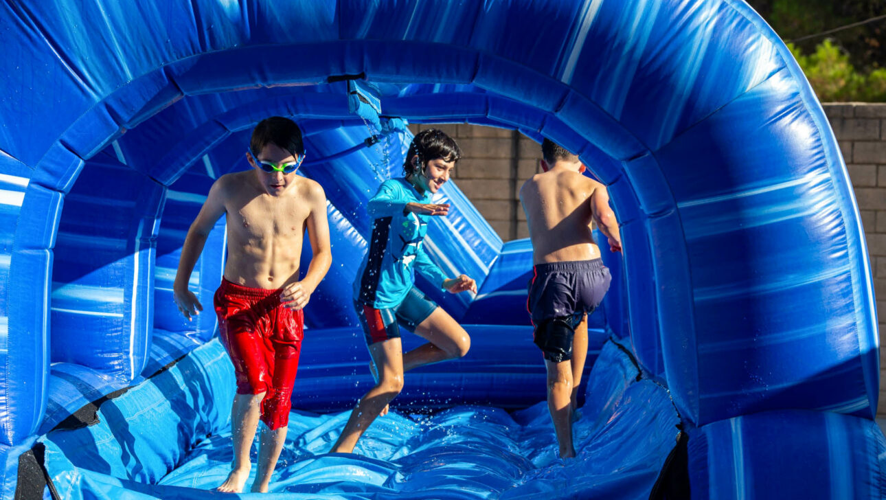three boys running on an inflatable water slide.