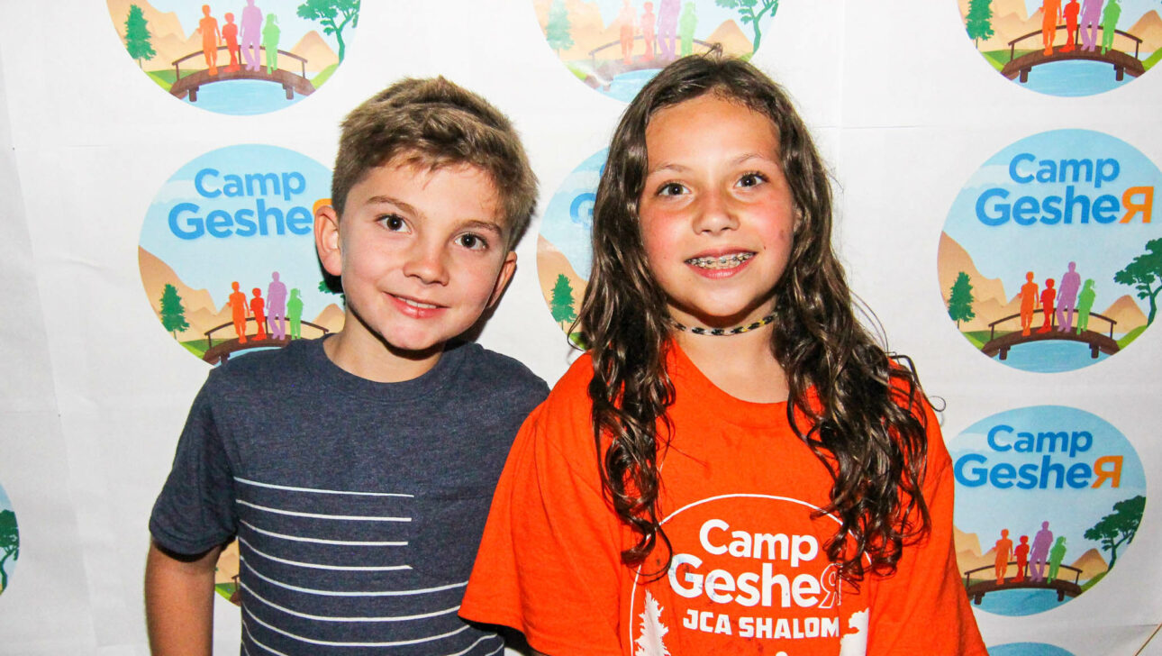 two kids smiling in front of a camp gesher background.