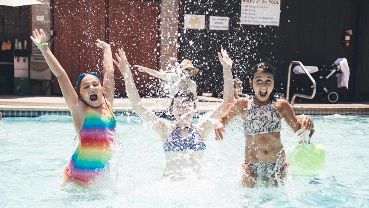 three girls splashing in a pool.