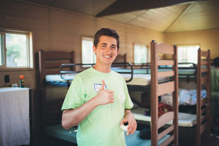 camp staff member giving a thumbs up sign inside a cabin.