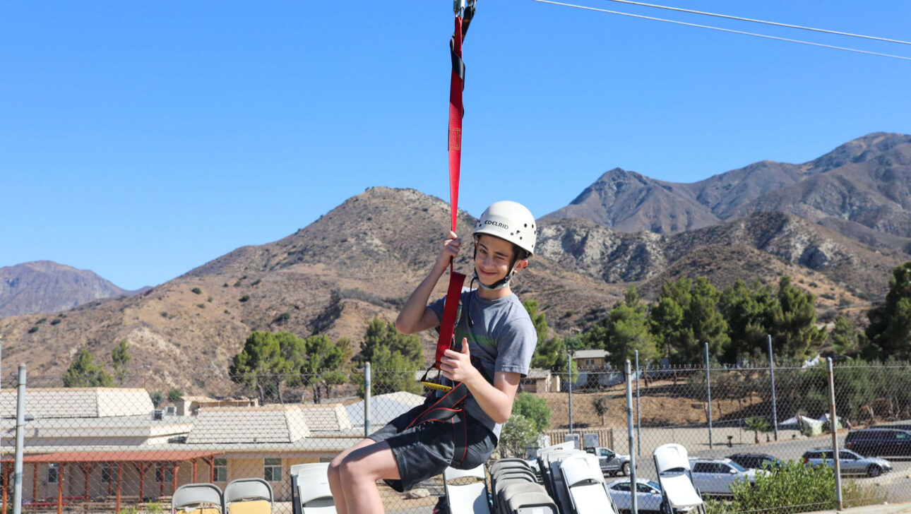 boy riding a zipline and giving a thumbs up sign.