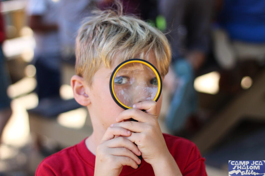 boy looking through a magnifying glass facing the camera.