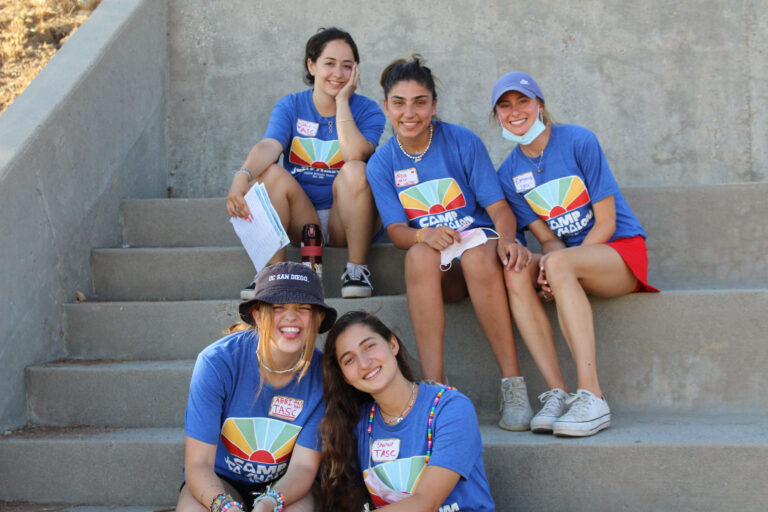 camp counselors in blue shirts sitting and smiling on some steps.