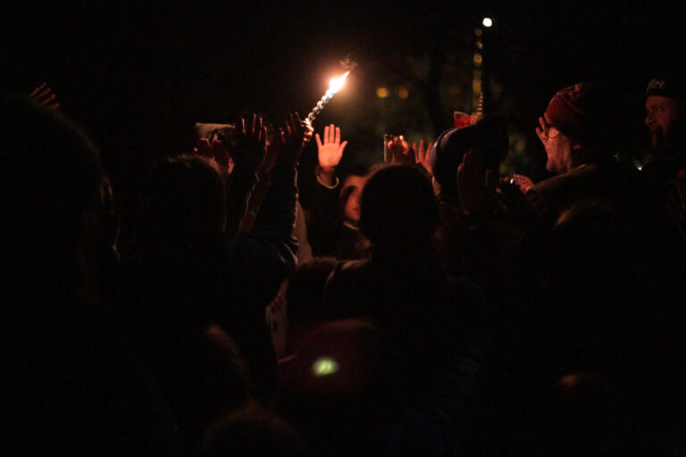 group of people huddled around a person holding a candle up at night.