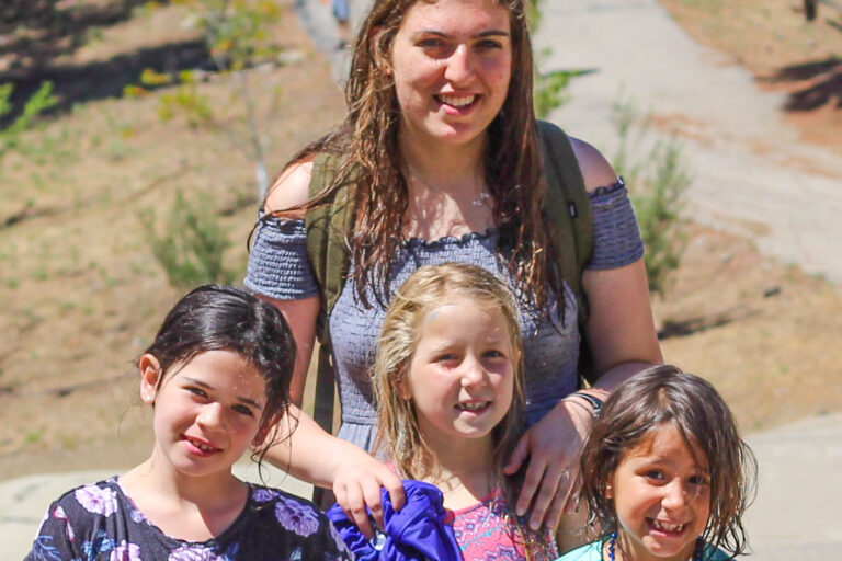 three girls smiling in front of a camp counselor.