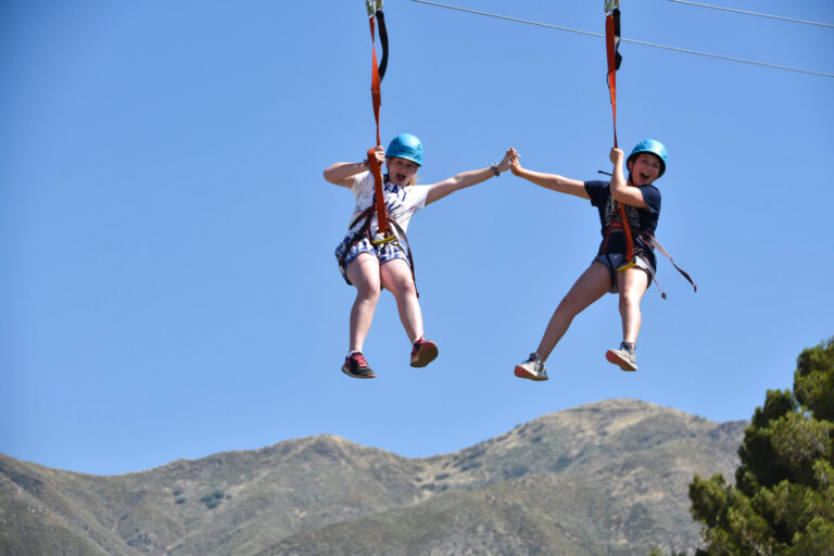 two girls high fiving on a zipline.