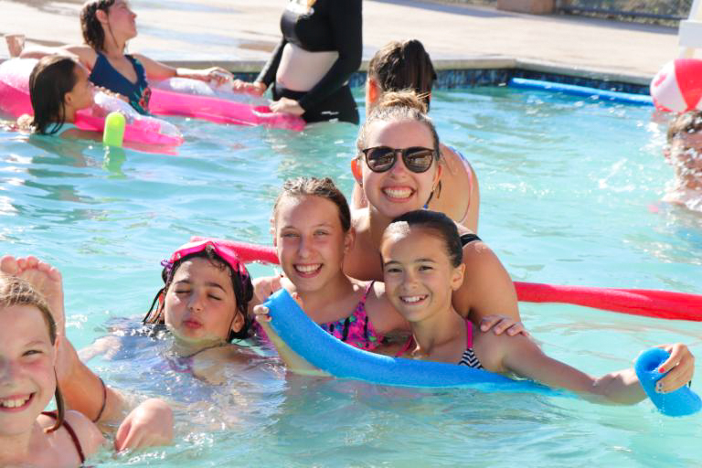 group of kids smiling and swimming in a pool with a camp counselor.