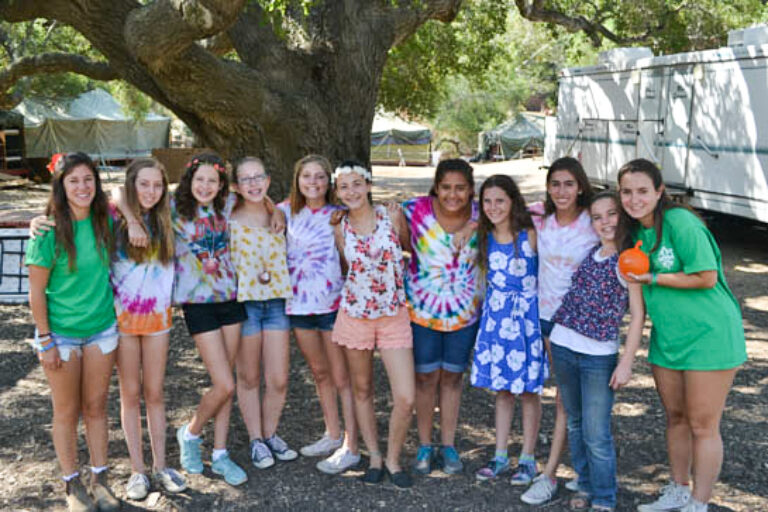 large group of girls standing shoulder to shoulder under a tree and smiling for the camera.