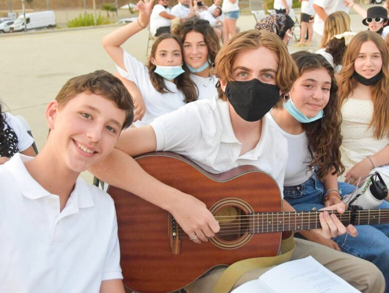 boy playing guitar with friends outside.