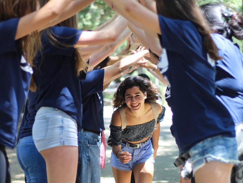 teen girl running through the arched arms of a group of camp counselors.