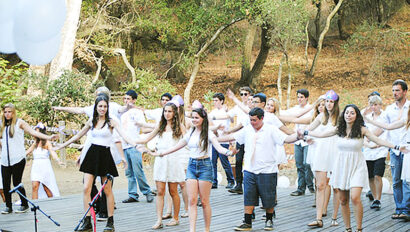 teens wearing white shirts performing on a stage outside.