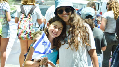 two girls smiling outside one holding a small israeli flag.