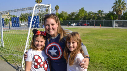 two girls smiling in front of a woman on a soccer field.