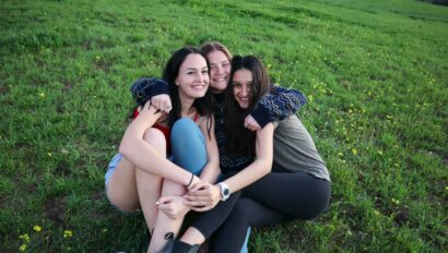 Three girls hugging and smile while sitting on the ground.