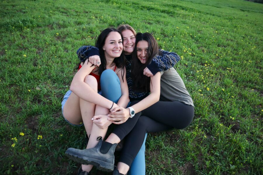 Three girls hugging and smile while sitting on the ground.