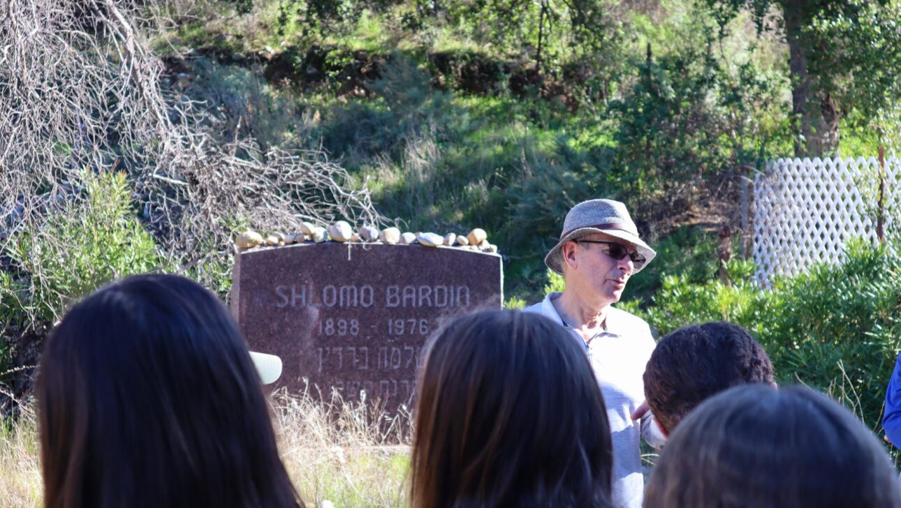man teaching something to kids who are looking at grave that says Shlomo Bardin.