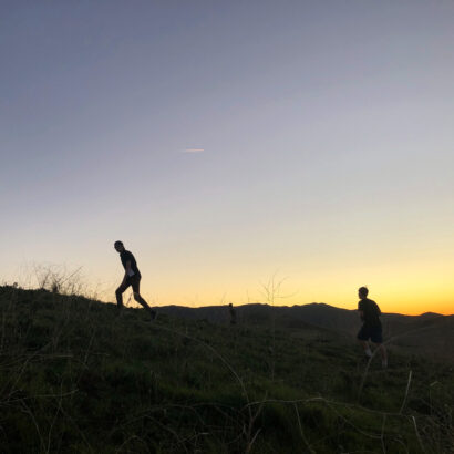 teens climbing up a hill in front of a sunset.