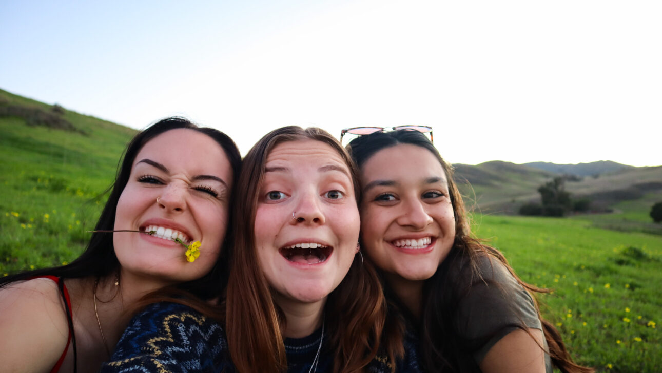 three teen girls smiling outside.
