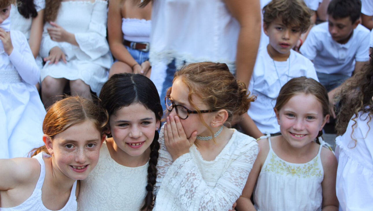 girl whispering something to another girl among a group of kids wearing white.